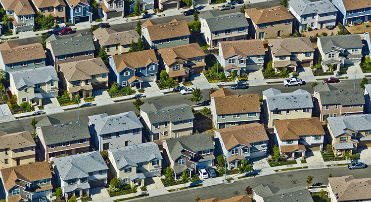 Aerial view of a suburban neighborhood showcasing rows of houses with different roof styles and cars parked along the streets, representing the residential housing market and mortgage options available in Lake Oswego, Oregon.
