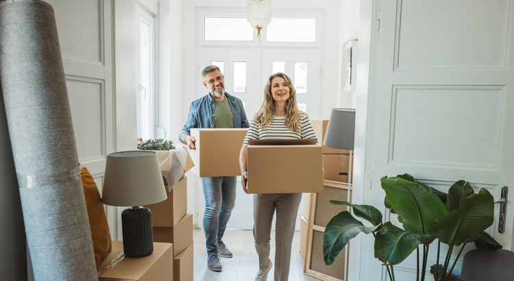 Happy couple moving into their new home, carrying boxes and smiling, symbolizing the long-term benefits of homeownership.