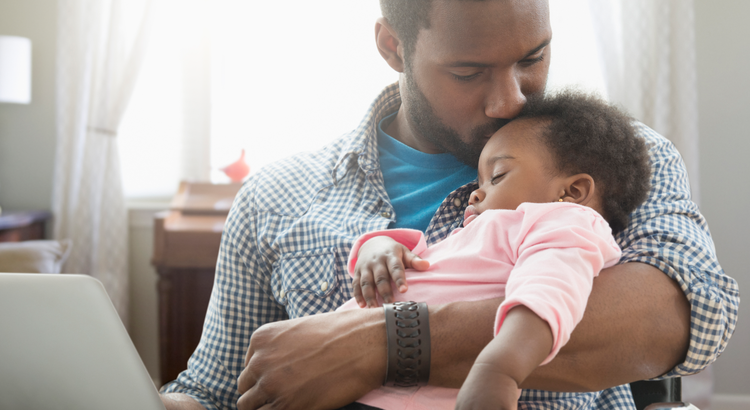 Father holding his sleeping child while working on a laptop, symbolizing personal reasons and motivations for moving.