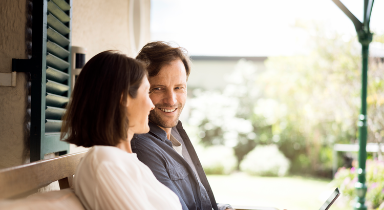 Smiling couple sitting on a porch, symbolizing the advantages of selling a house when inventory is low.