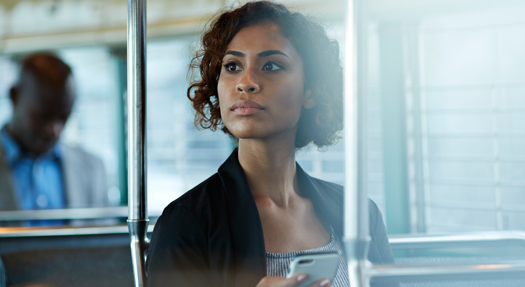 Young woman thoughtfully looking out a window while holding a smartphone, symbolizing stability in the housing market despite foreclosures and bankruptcies.