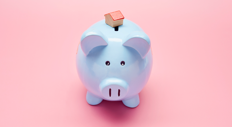 Blue piggy bank with a small house model on top, symbolizing saving for a home.