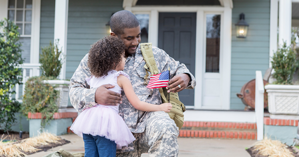 Military servicemember hugging a child while holding an American flag, symbolizing VA loans and homeownership.
