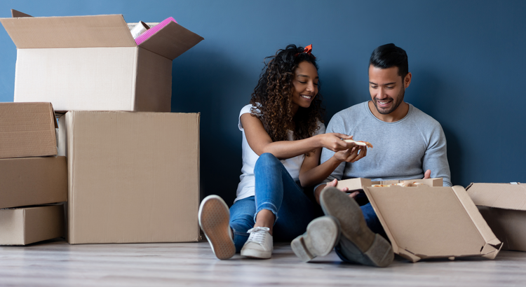 Couple sitting on the floor surrounded by moving boxes, symbolizing the continuation of home purchases despite affordability challenges.