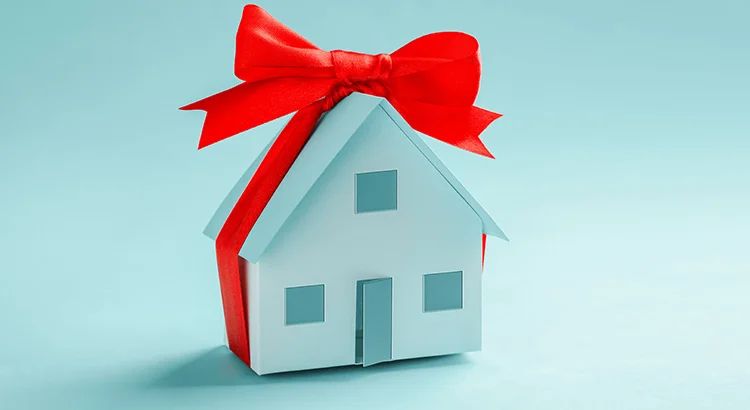 Model house with a red bow, symbolizing a home as a top item on buyers' wish lists during the holiday season.