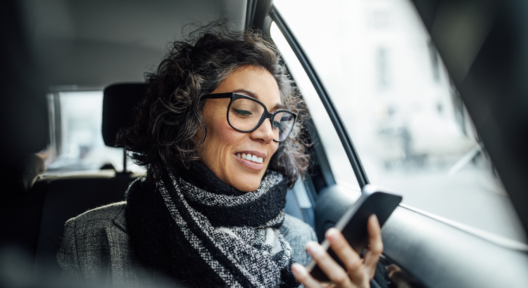Woman smiling while looking at her smartphone in a car, symbolizing staying informed about home prices and market trends.