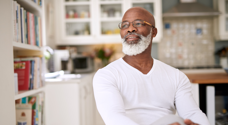 Older man with glasses and a beard smiling while sitting in a bright, modern kitchen.