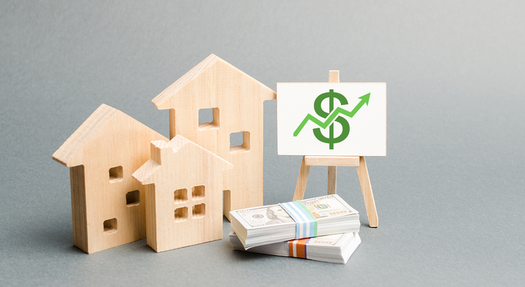 Wooden house models and stacks of cash with a chart showing financial growth, symbolizing the financial benefits of homeownership.