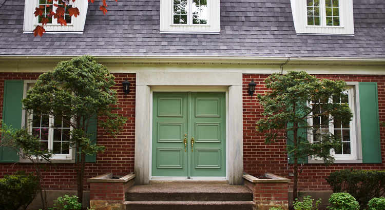 Front view of a brick house with a green door and well-manicured landscaping, symbolizing curb appeal.